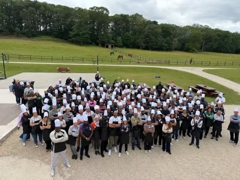 Grand groupe en toques de chef posant en plein air devant un pré avec chevaux