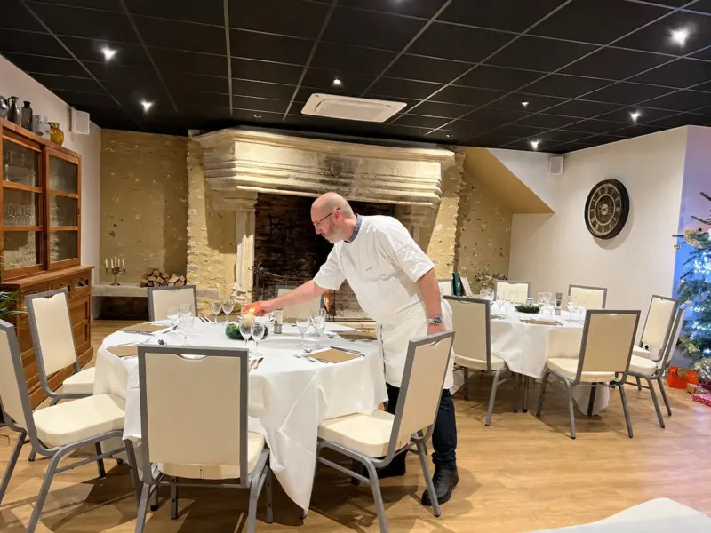 Chef dressant une table ronde festive devant une cheminée en pierre