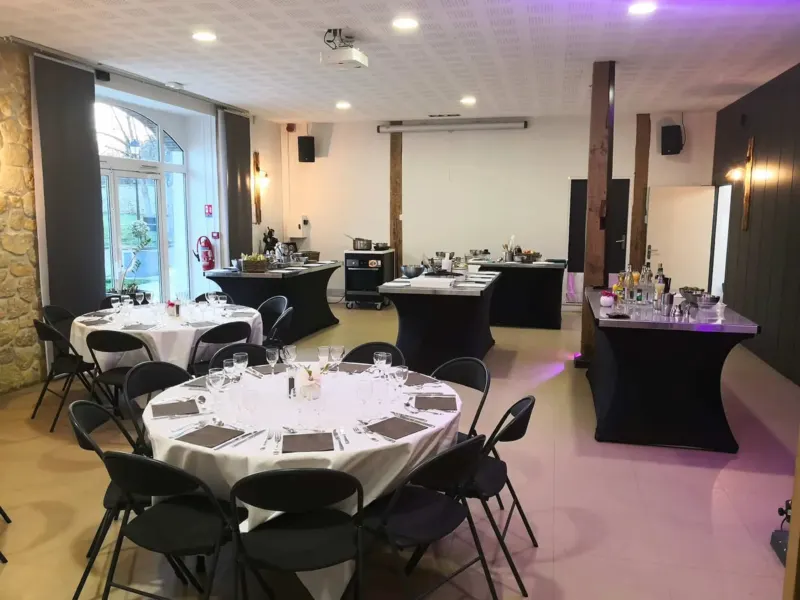Salle dressée avec tables rondes et plans de cuisine noirs en fond