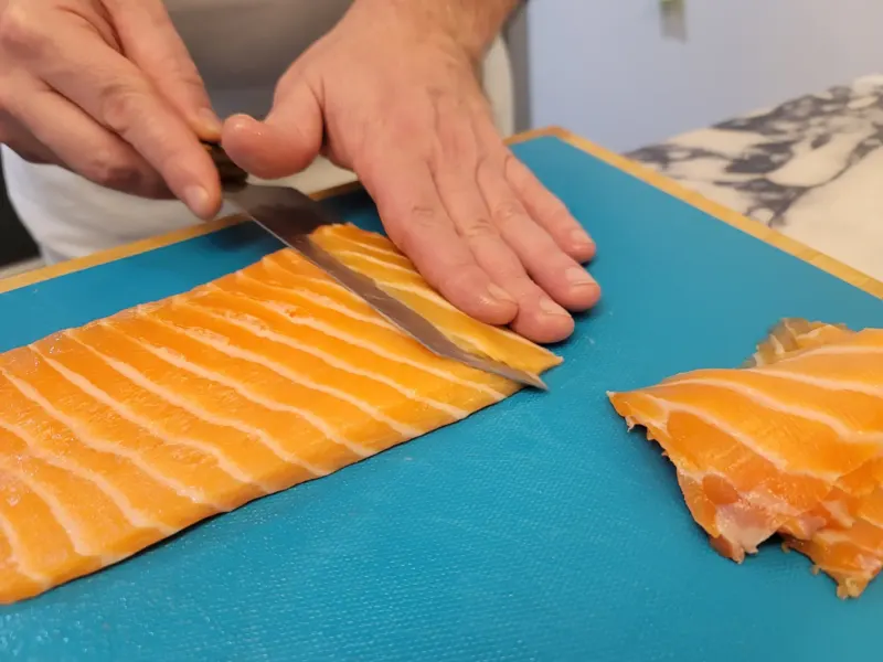 Mains tranchant un pavé de saumon au couteau sur planche bleue